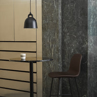 "Black pendant light, marble grey wall, gold-patterned cabinetry, and a brown chair beside a round black table."