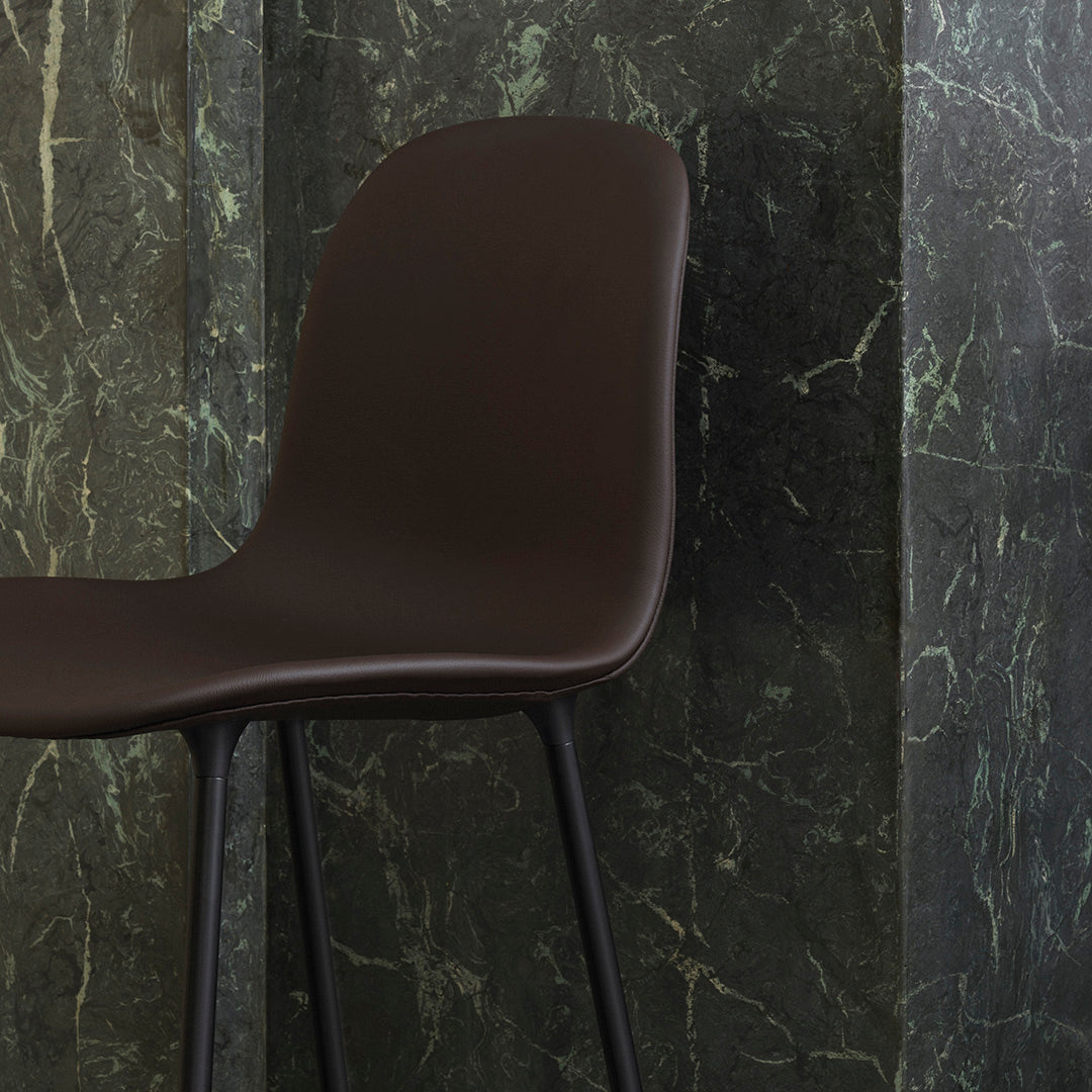 Stylish brown molded chair against a dark green marbled backdrop, highlighting sleek lines and modern design.