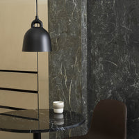 "Matte black pendant lamp against textured dark green marble and warm beige wall, featuring a sleek black marble table."