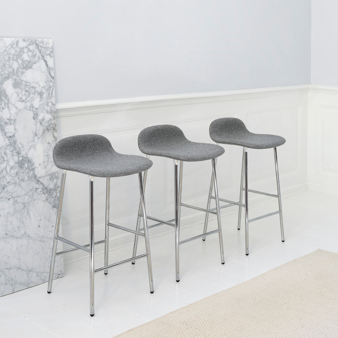 Gray upholstered bar stools with sleek chrome legs, set against a minimalist backdrop of light colors and marble pattern.