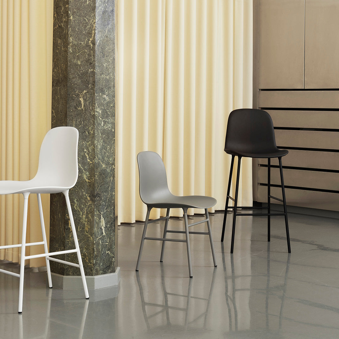 Modern chairs in white, gray, and black against a soft yellow curtain backdrop, showcasing sleek design and minimalist aesthetics.