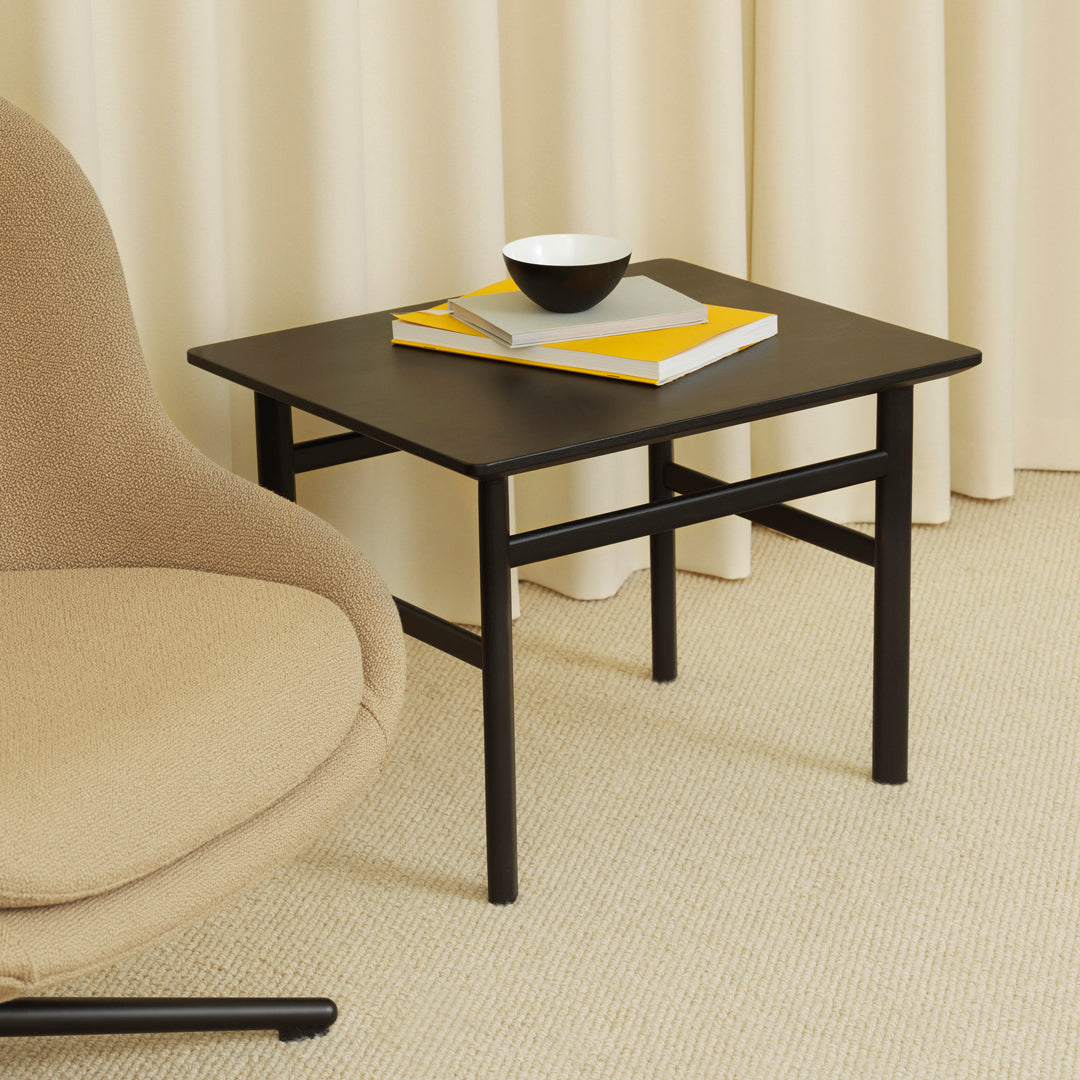 Black square side table with minimalist design, paired with a white bowl and yellow accents, set against neutral tones.