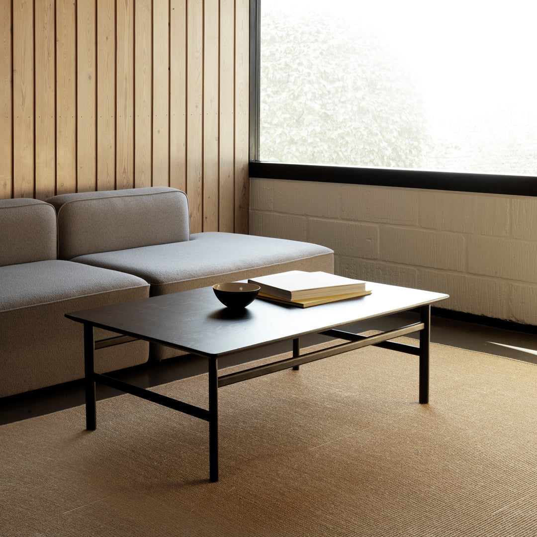 Modern black coffee table with sleek lines, complemented by a neutral gray sofa and warm wooden walls.