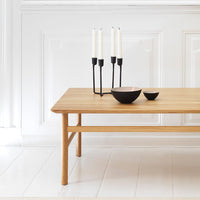 Natural wood table with a smooth finish, featuring black candlesticks and bowls for a modern contrast in a bright setting.