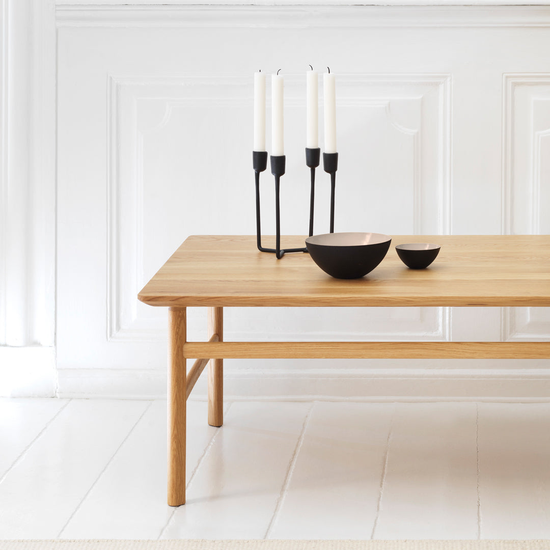 Wooden table in natural finish with black candle holder and bowls, set against a soft white background.