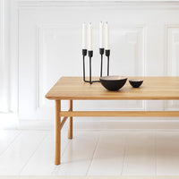 Wooden table in natural finish with black candle holder and bowls, set against a soft white background.
