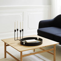 Stylish black candles on a round black tray atop a light wood coffee table, accented by a dark blue sofa.
