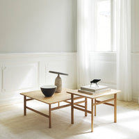 "Natural wood coffee tables with a light finish, complemented by a black bowl and neutral decor against soft gray walls."