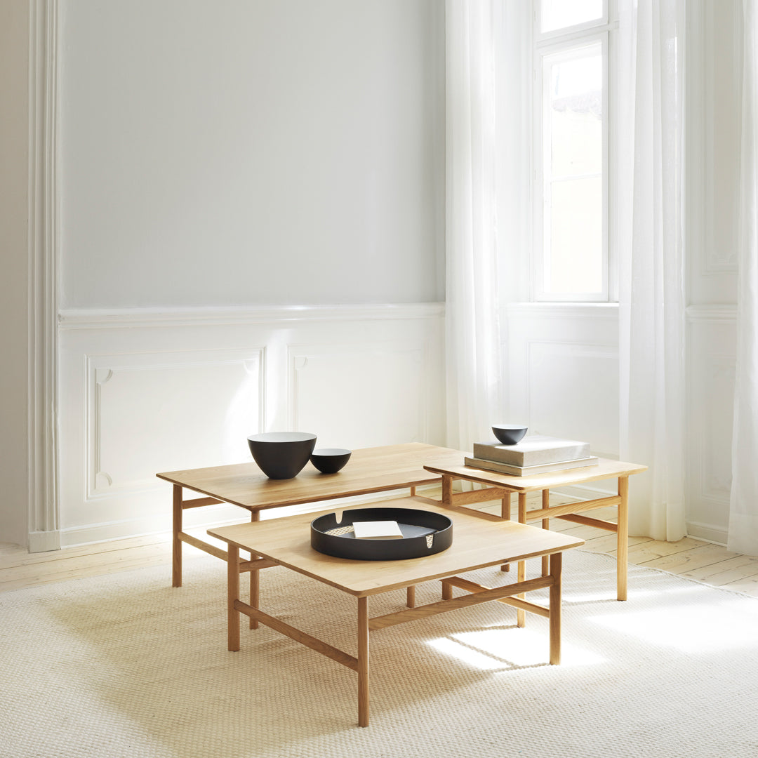 Set of light wood coffee tables with black geometric bowls on a soft cream rug and bright, airy room.