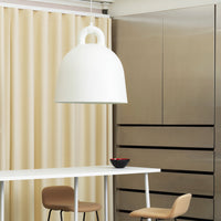 White bell-shaped pendant light against beige curtains and sleek stainless steel wall. Simple, modern design.