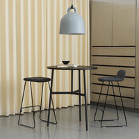 "Modern black bar table and stools with grey pendant light against soft yellow curtains."