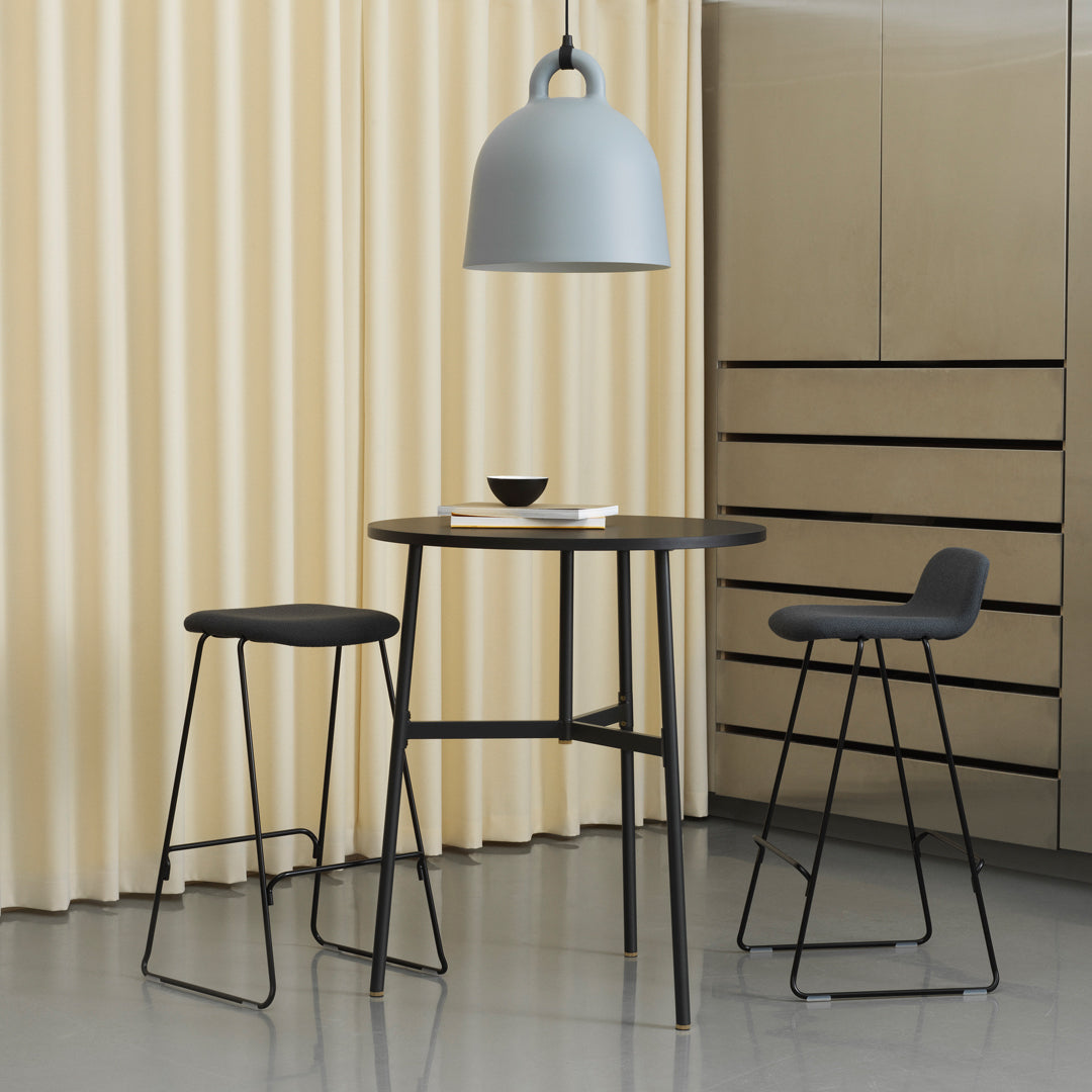 "Modern black bar table and stools with grey pendant light against soft yellow curtains."