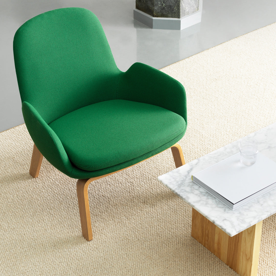 Green upholstered armchair with a smooth, modern design and natural wood legs, set against a neutral rug.