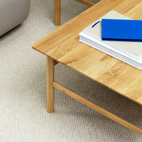 Light wood coffee table with a smooth finish, styled with blue and neutral-toned books on a textured light carpet background.