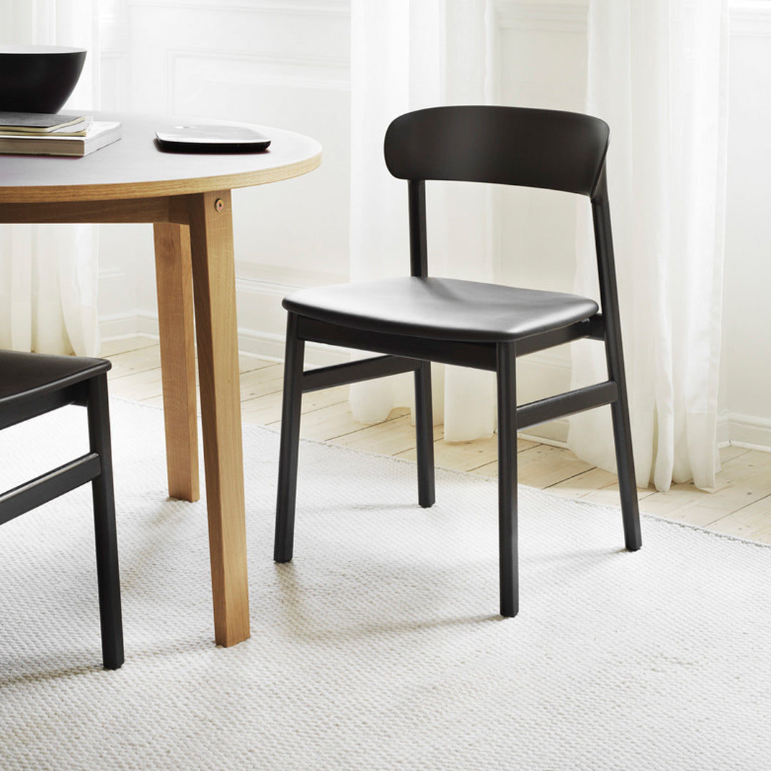 Black wooden chair with smooth finish, paired with a round wooden table on a light textured rug.