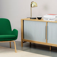 Green chair with curved design, light wood cabinet with ribbed grey doors, gold lamp, minimalist decor.