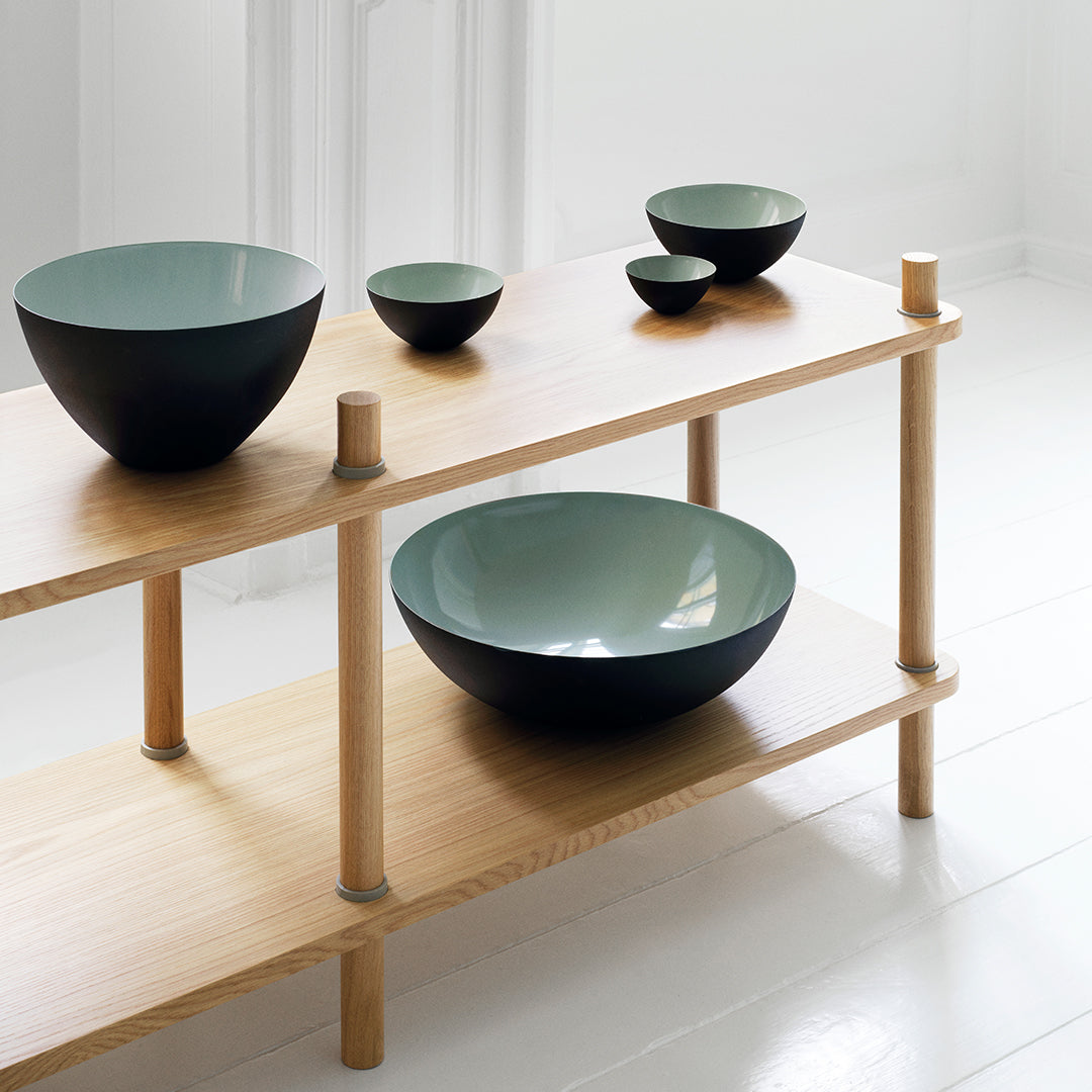 Set of modern bowls in matte black and light green, arranged on a minimalist wooden shelf.