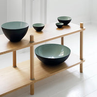 Set of modern bowls in matte black and light green, arranged on a minimalist wooden shelf.