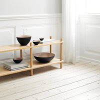 "Set of black and gold bowls with smooth finishes displayed on a light wooden shelf in a minimalist setting."