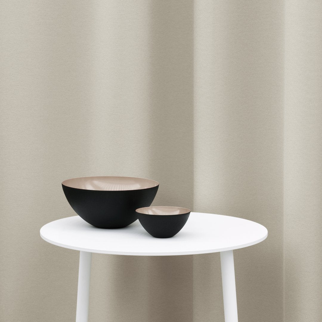 Two modern bowls in matte black with a light beige interior, displayed on a white table against a neutral backdrop.