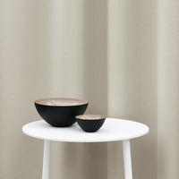 Two modern bowls in matte black with a light beige interior, displayed on a white table against a neutral backdrop.