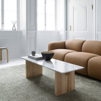 Modern marble-top coffee table with light wood legs, set against a soft green rug and warm beige sofa.