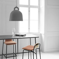 Grey pendant light over a minimalist table with black frame; soft coral-colored chairs contrast against a white backdrop.