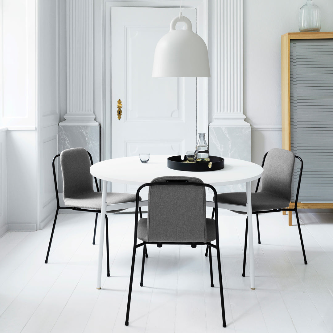 Round white dining table with four grey chairs, set against a minimalist white and neutral-toned backdrop.