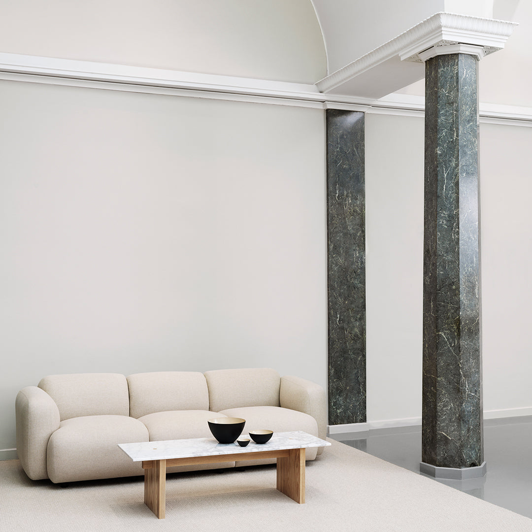 Soft beige sofa paired with a sleek white marble table and dark green marble pillars, set against a neutral wall.
