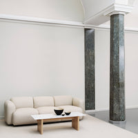 Soft beige sofa paired with a sleek white marble table and dark green marble pillars, set against a neutral wall.