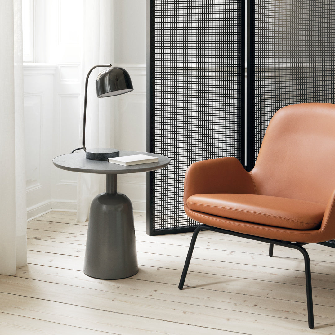 Modern round grey side table next to a sleek orange armchair, featuring minimalistic design and clean lines.