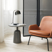 Modern round grey side table next to a sleek orange armchair, featuring minimalistic design and clean lines.