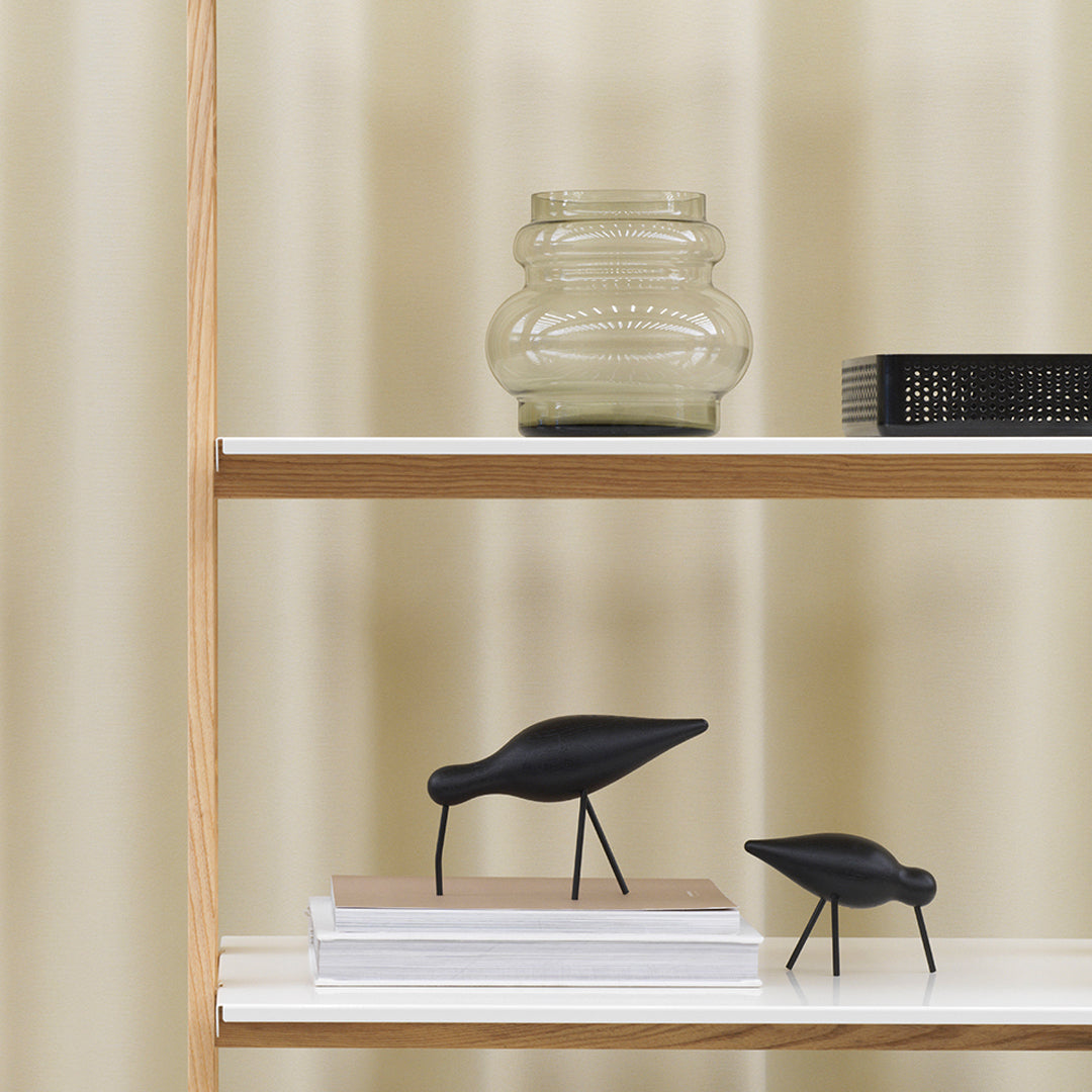 Black decorative birds on a shelf, soft beige curtains in the background, with a glass vase and patterned book.