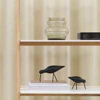 Black decorative birds on a shelf, soft beige curtains in the background, with a glass vase and patterned book.