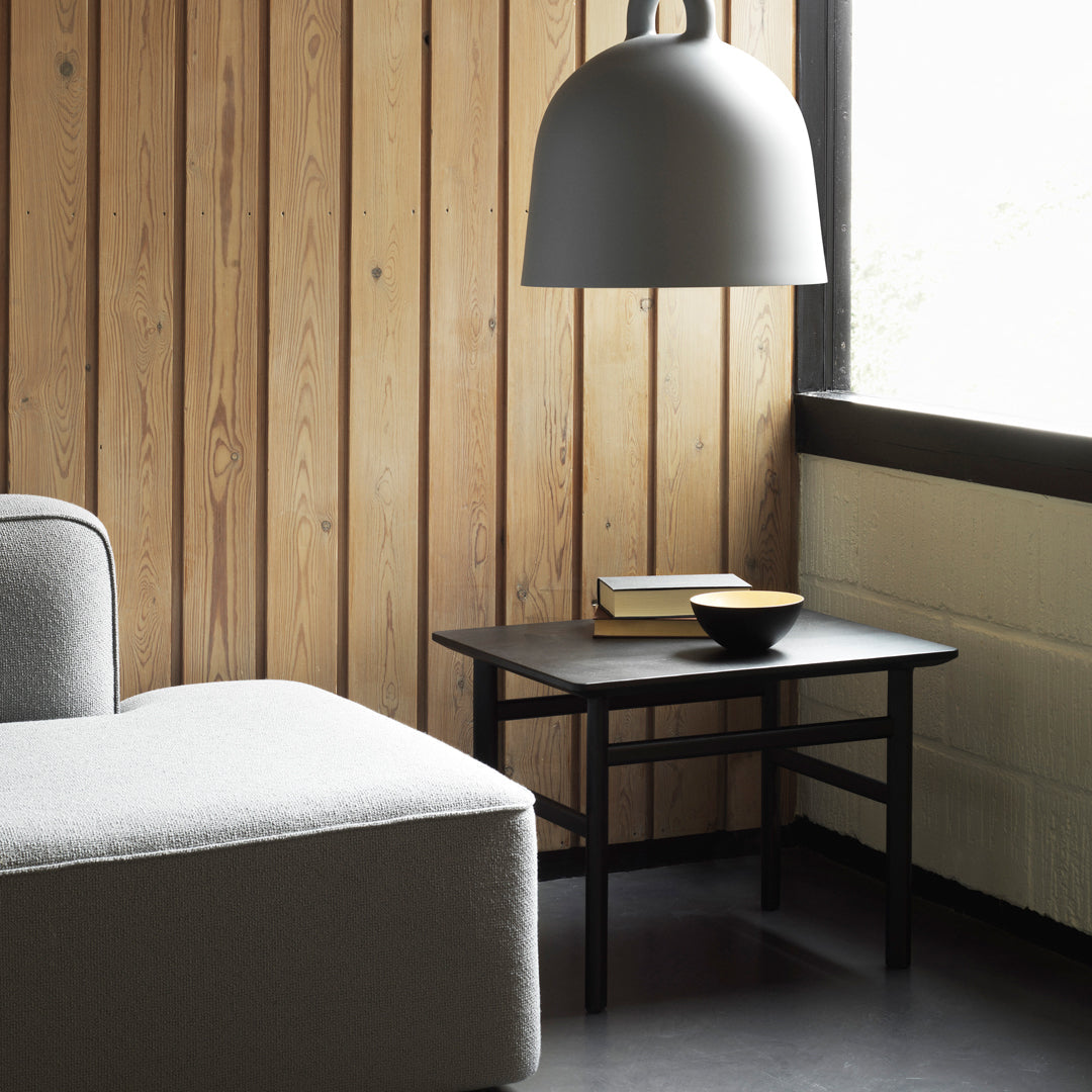 "Modern black side table with clean lines, featuring a minimalist design against a warm wooden wall and gray accents."