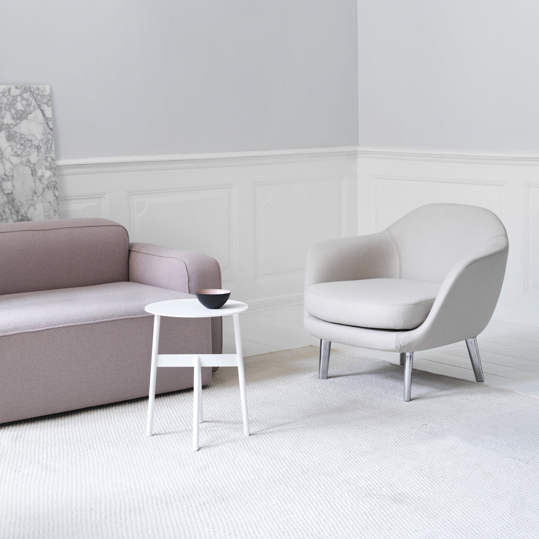 Light gray armchair with smooth curves beside a soft pink sofa, set against a minimalist white backdrop.
