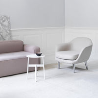 Light gray armchair with smooth curves beside a soft pink sofa, set against a minimalist white backdrop.