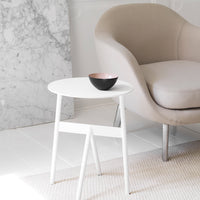 "Stylish white round table with minimalist design, paired with a soft beige chair and a black bowl embellished with pink."