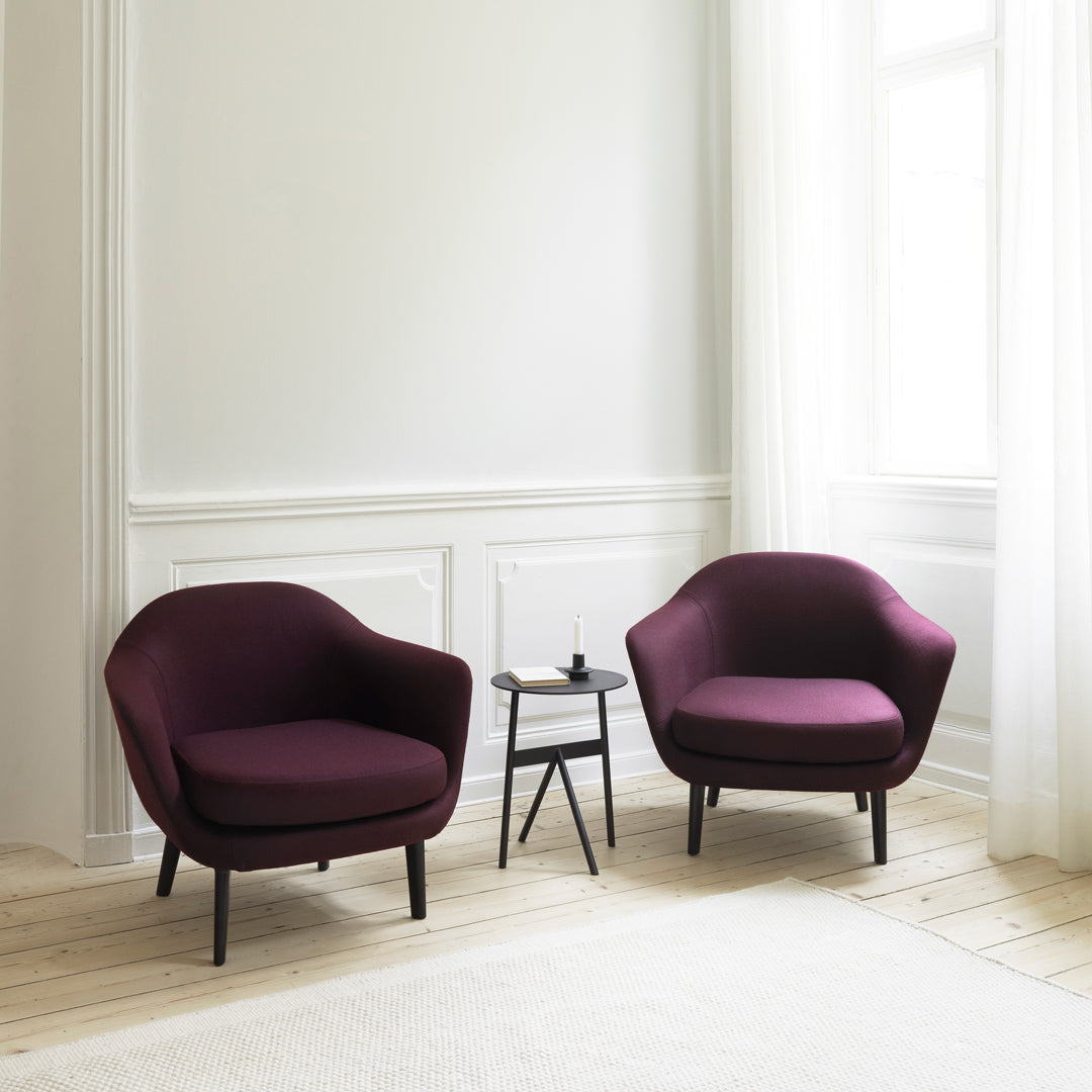 Two modern chairs in rich purple fabric with black legs, set against a light, airy room with white curtains.