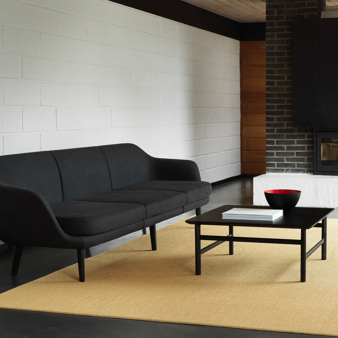 Black modern sofa on a neutral-toned rug, complemented by a black coffee table and vibrant red bowl accent.