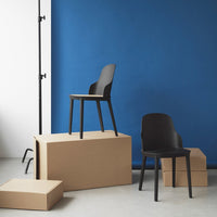 Modern black chairs stacked on cardboard boxes against a vibrant blue backdrop, showcasing minimalist design.