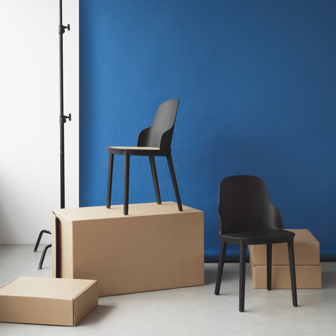 Modern black chairs stacked on cardboard boxes against a vibrant blue backdrop, showcasing minimalist design.