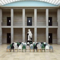 Colorful chairs in various shades of green, gray, and white arranged in a circular pattern around a central statue.
