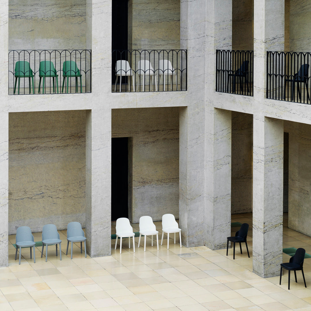 Collection of minimalist chairs in green, gray, white, and black arranged in an architectural space with clean lines.