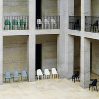 Collection of minimalist chairs in green, gray, white, and black arranged in an architectural space with clean lines.