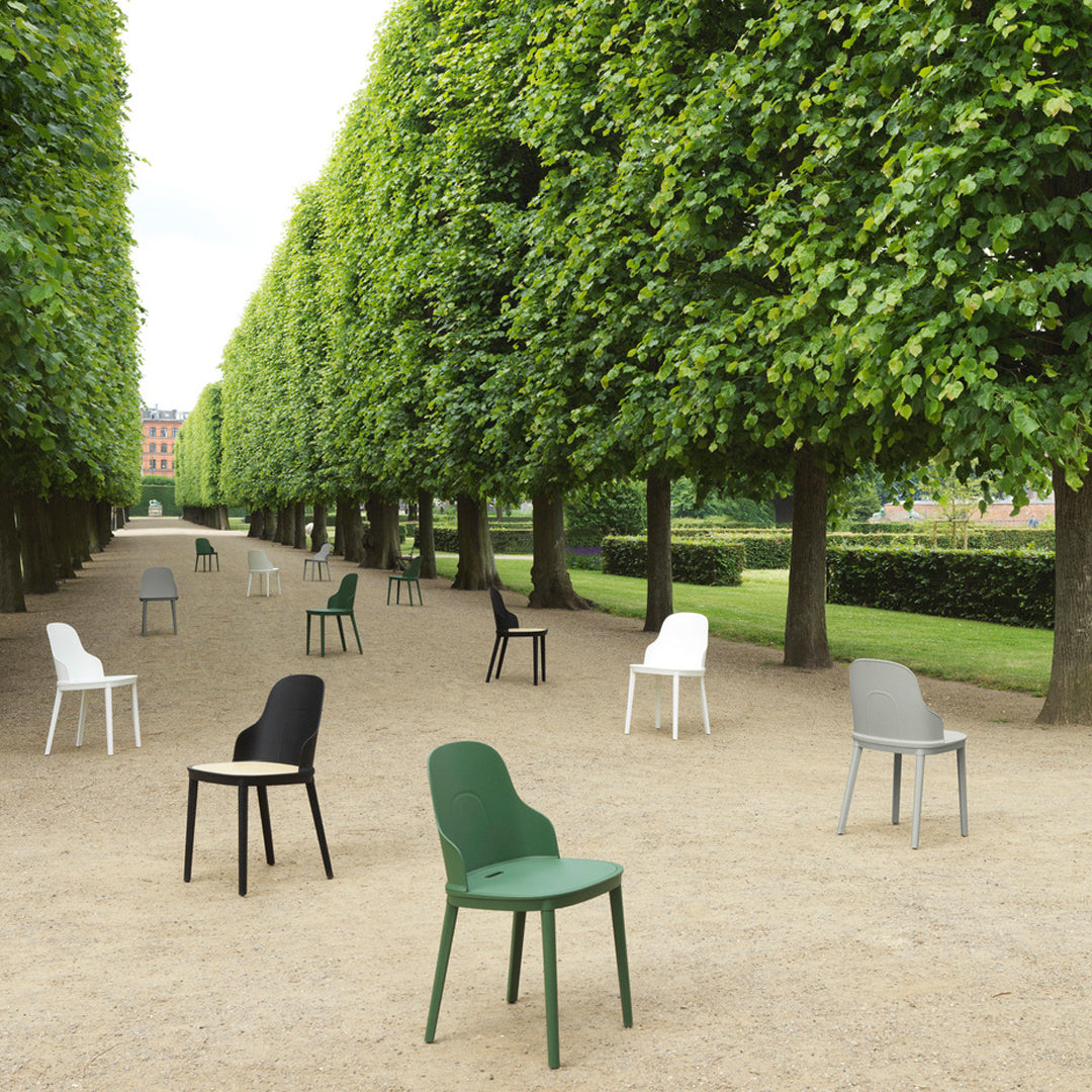 Colorful chairs in green, black, white, and gray arranged on a tree-lined pathway, featuring minimalist designs.