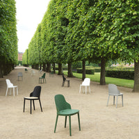 Colorful chairs in green, black, white, and gray arranged on a tree-lined pathway, featuring minimalist designs.