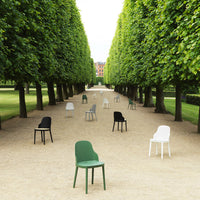 Colorful outdoor chairs in green, black, white, and grey arranged in a scenic row under lush green trees.