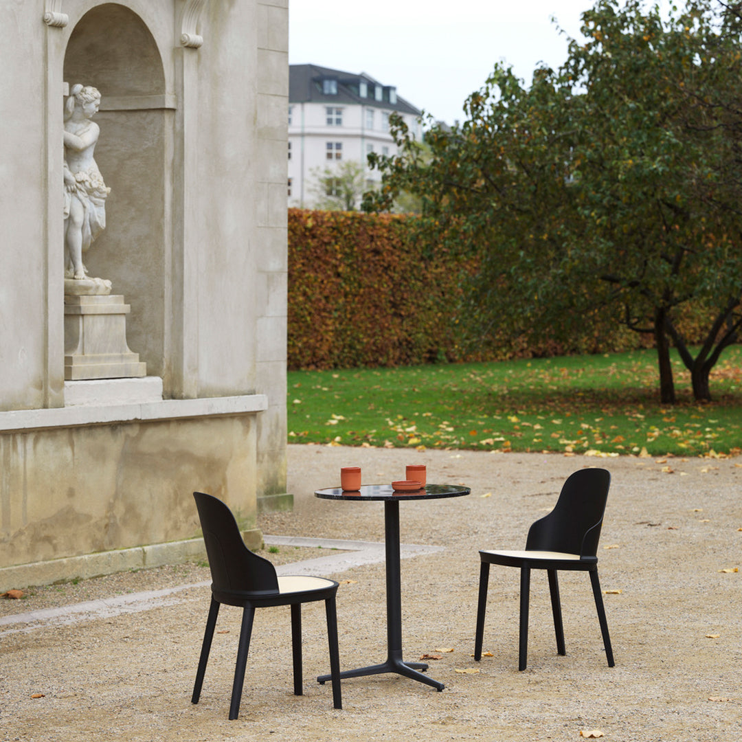 Black chairs and round black table set against a neutral backdrop, surrounded by autumn foliage.