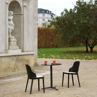 Black chairs and round black table set against a neutral backdrop, surrounded by autumn foliage.